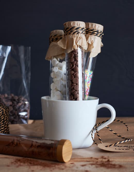 Éprouvettes en verre remplies de garnitures pour chocolat chaud placées dans une chope blanche.