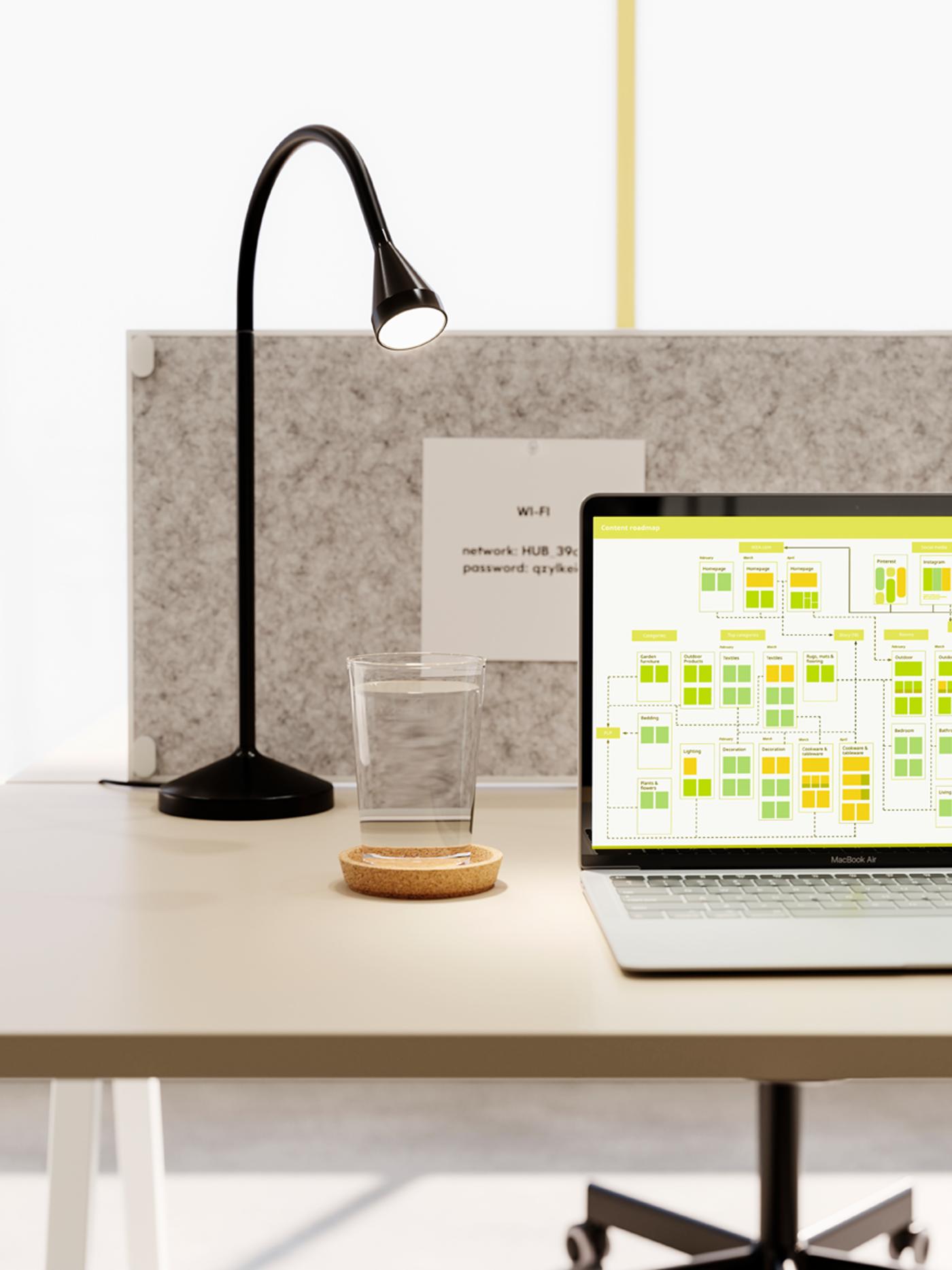 Es ist ein minimalistischer Arbeitsplatz mit einem Laptop, einer schwarzen NÄVLINGE LED-Arbeitsleuchte und einem Glas Wasser zu sehen.