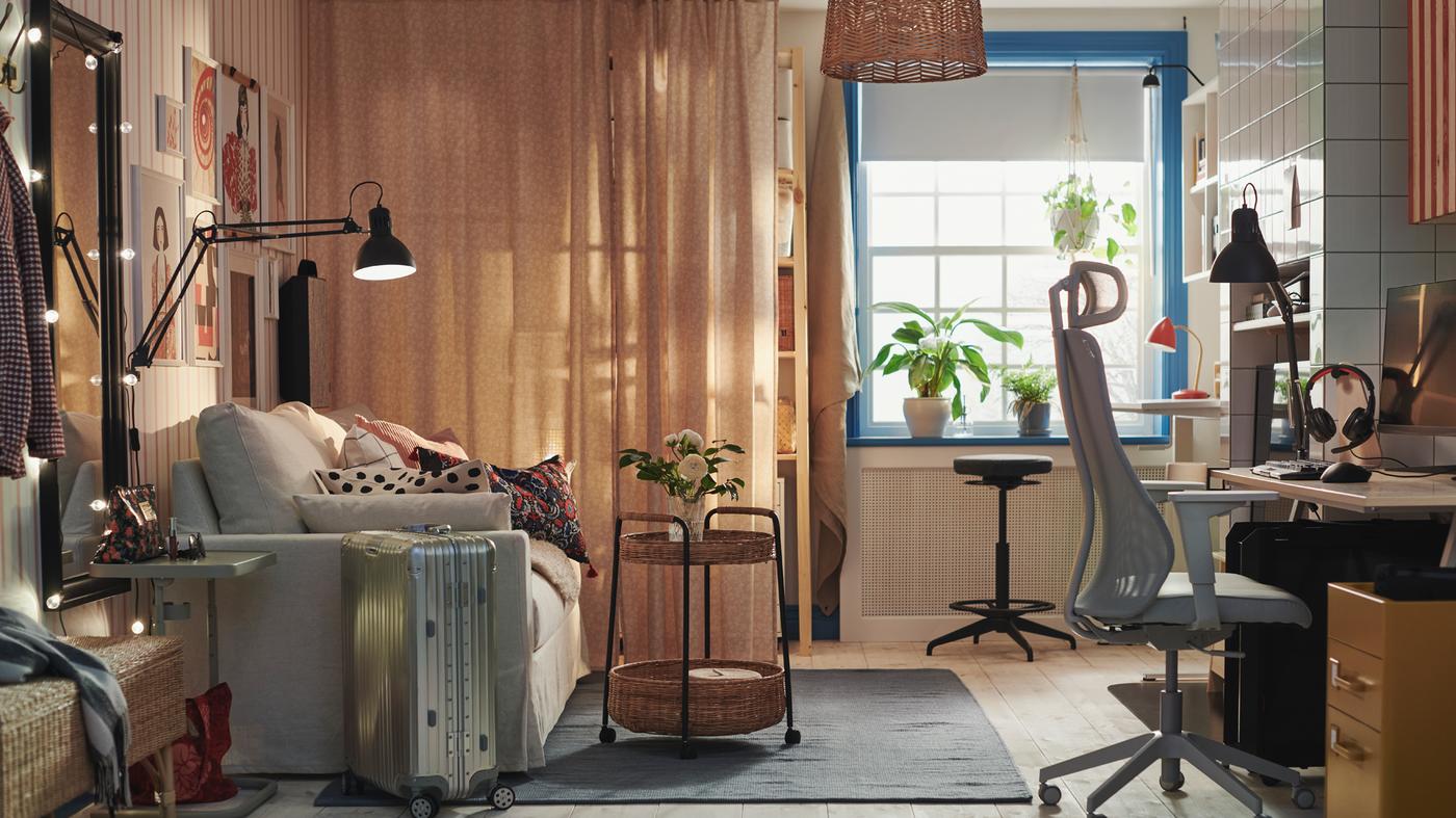 Es ist ein Raum mit einem Rolltisch mit Aufbewahrung zu sehen, der auf einem Teppich vor einem HYLTARP Bettsofa und in Nähe einer aktiven LIDKULLEN Sitz-/Stehstütze steht.