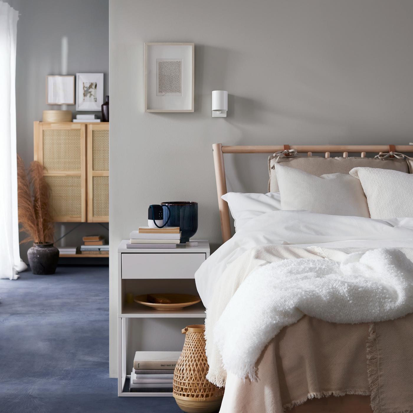 Es ist ein Schlafzimmer mit einem hellen Holzbett zu sehen, das mit ÄNGSLILJA Bettwäsche bezogen ist. Darüber hängt eine weisse NYMÅNE Wand-/Leseleuchte.