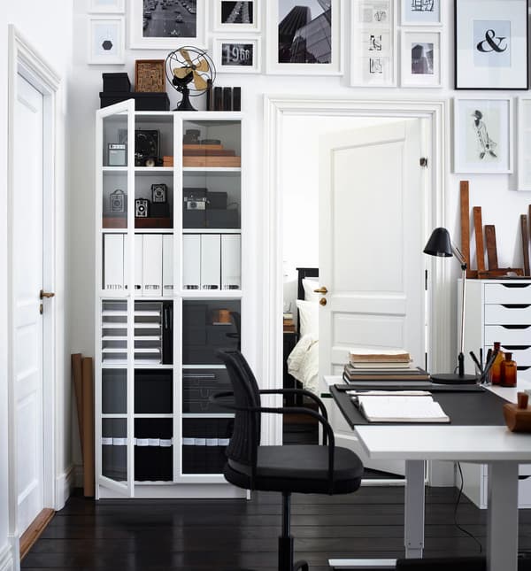 Espace de travail à domicile présentant du rangement, quantité d’œuvres exposées au mur, un bureau et une chaise.