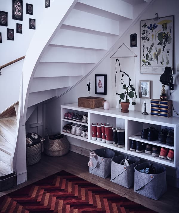 Espace ouvert sous l’escalier avec paniers de rangement et étagères pour les bottes et chaussures.