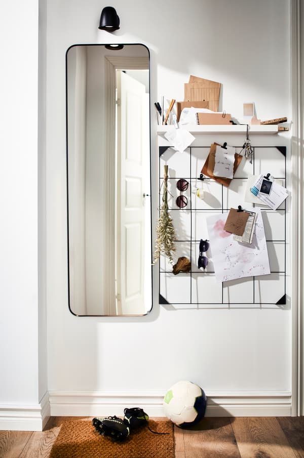 Espejo largo junto a un tablero de pared con notas, cartas y decorativos.