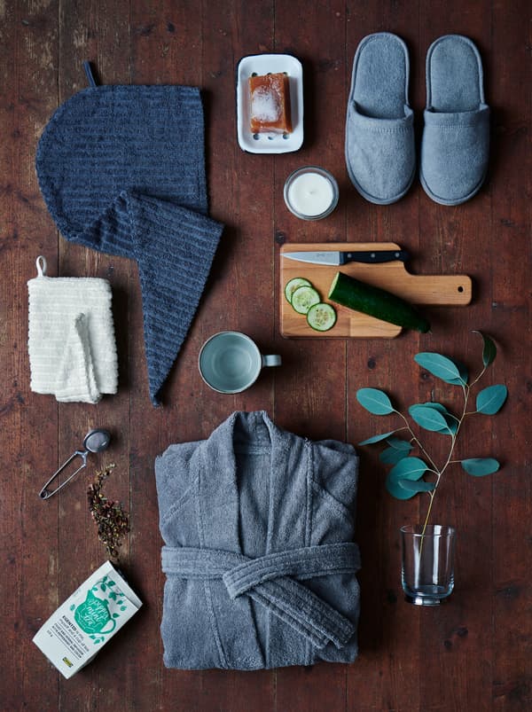 Essentials for a spa day at home such as a ROCKÅN bath robe and EGENTID tea are set on a dark wooden floor.
