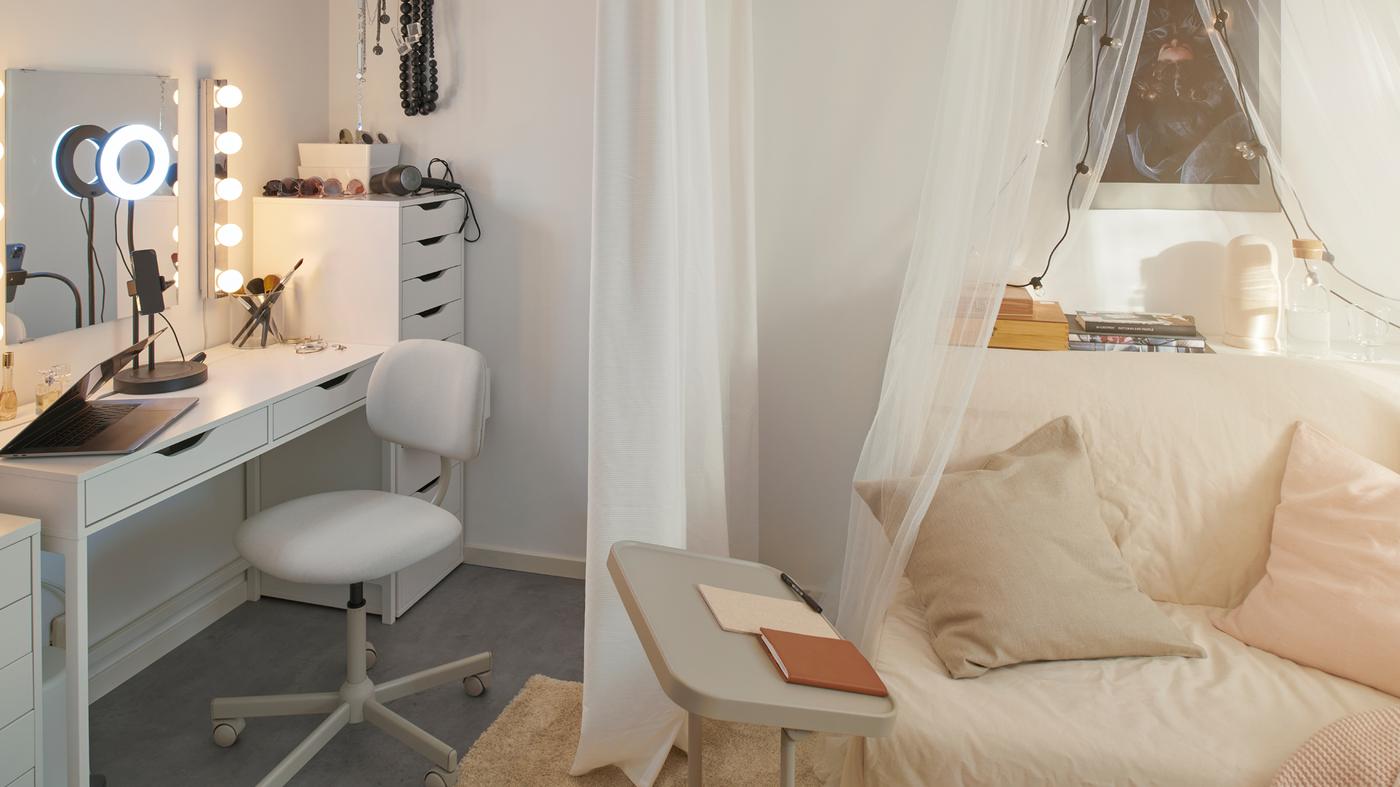 Et ALEX skrivebord og et ALEX skuffeelement danner et område til påklædning. En BJÖRKÅSEN støtte til bærbar computer og en LYCKSELE HÅVET sovesofa står i nærheden.