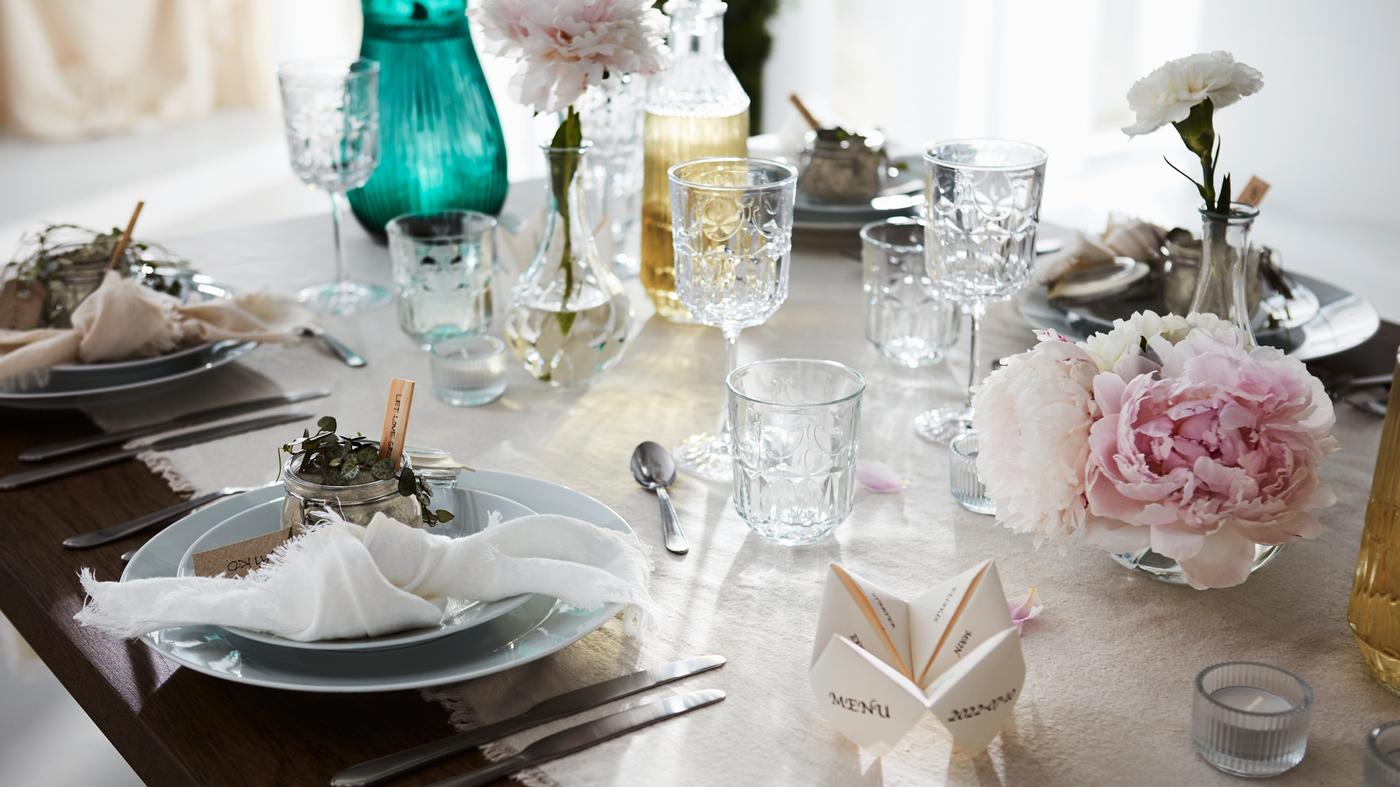Et festligt bord dækket til en formel lejlighed med en let dug, fine glas, tallerkener, bestik og blomsterdekorationer.
