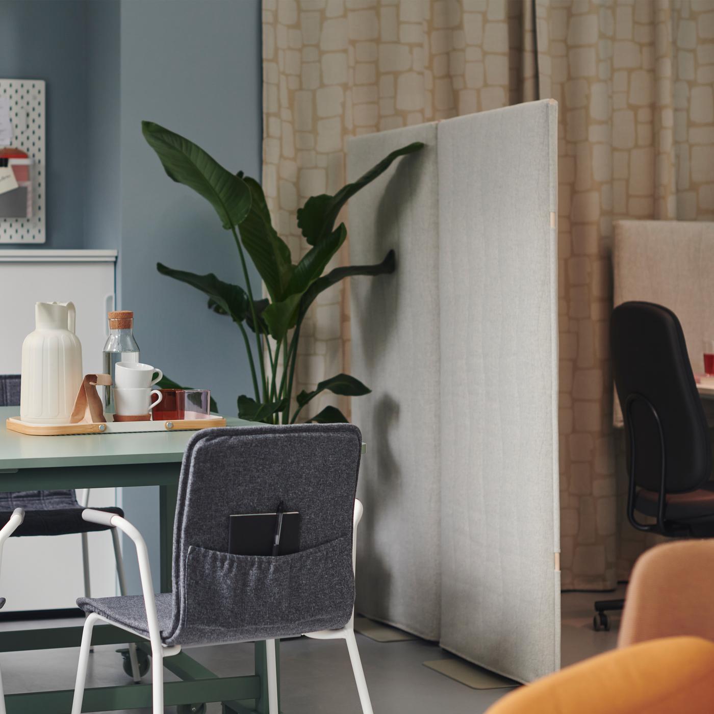 Et lille kontor med blå vægge og beige gardiner, en grå LÄKTARE stol med en lomme og en stor, grøn plante i hjørnet. 