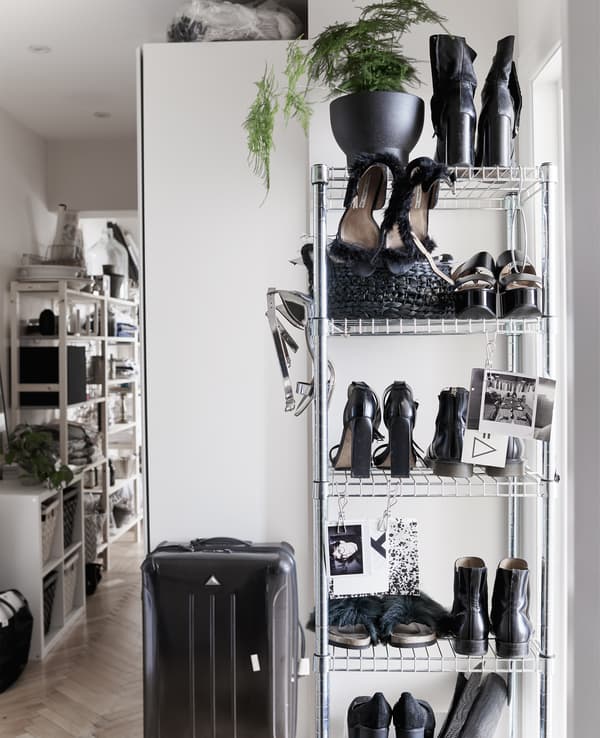 Étagère ouverte haute garnie de chaussures et valise noire.