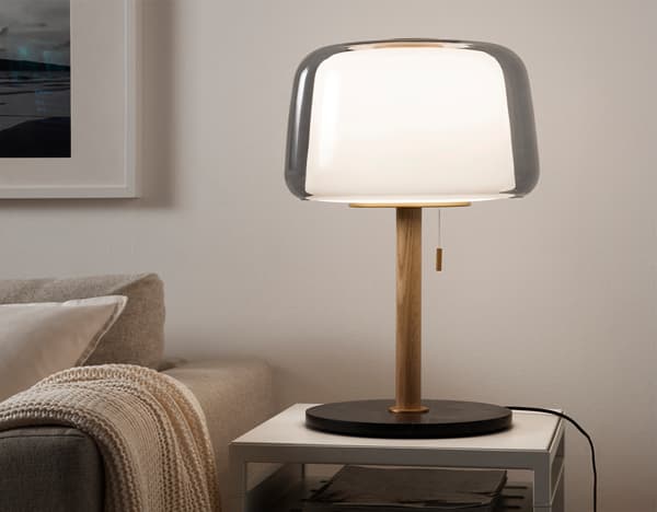 EVEDAL table lamp lit up on a coffee table beside a sofa in the living room, to illustrate IKEA home design service