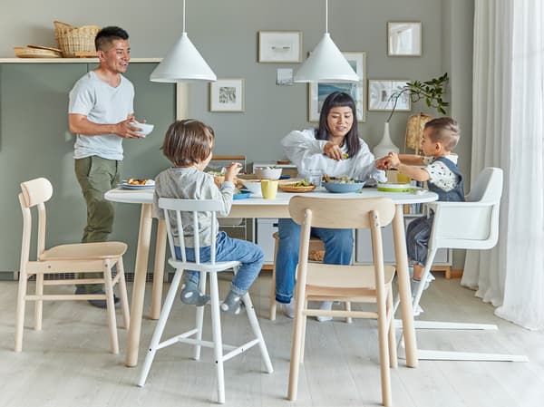 Famille à la salle à manger La maman et les deux enfants sont assis à la table alors que le papa leur apporte un bol.