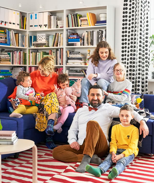 Famille nombreuse sur un canapé d'angle bleu, devant des bibliothèques.