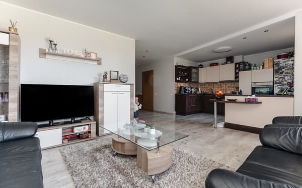 Family living room before the makeover, viewed towards the open-plan kitchen with brown and beige cabinets.						