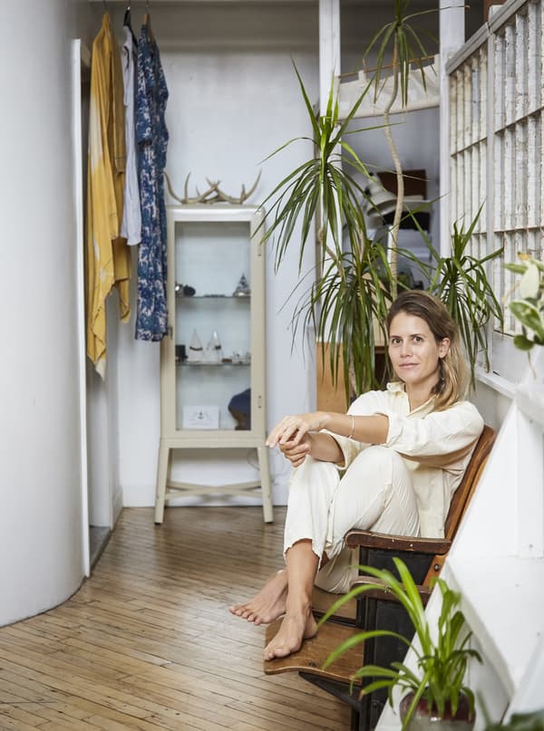 Femme assise dans un fauteuil dans une pièce garnie de plantes.