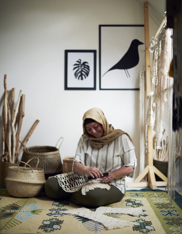 Femme assise par terre, en train de faire du macramé.