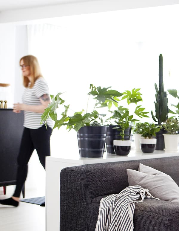 Femme debout dans un espace monochrome et garni de verdure.