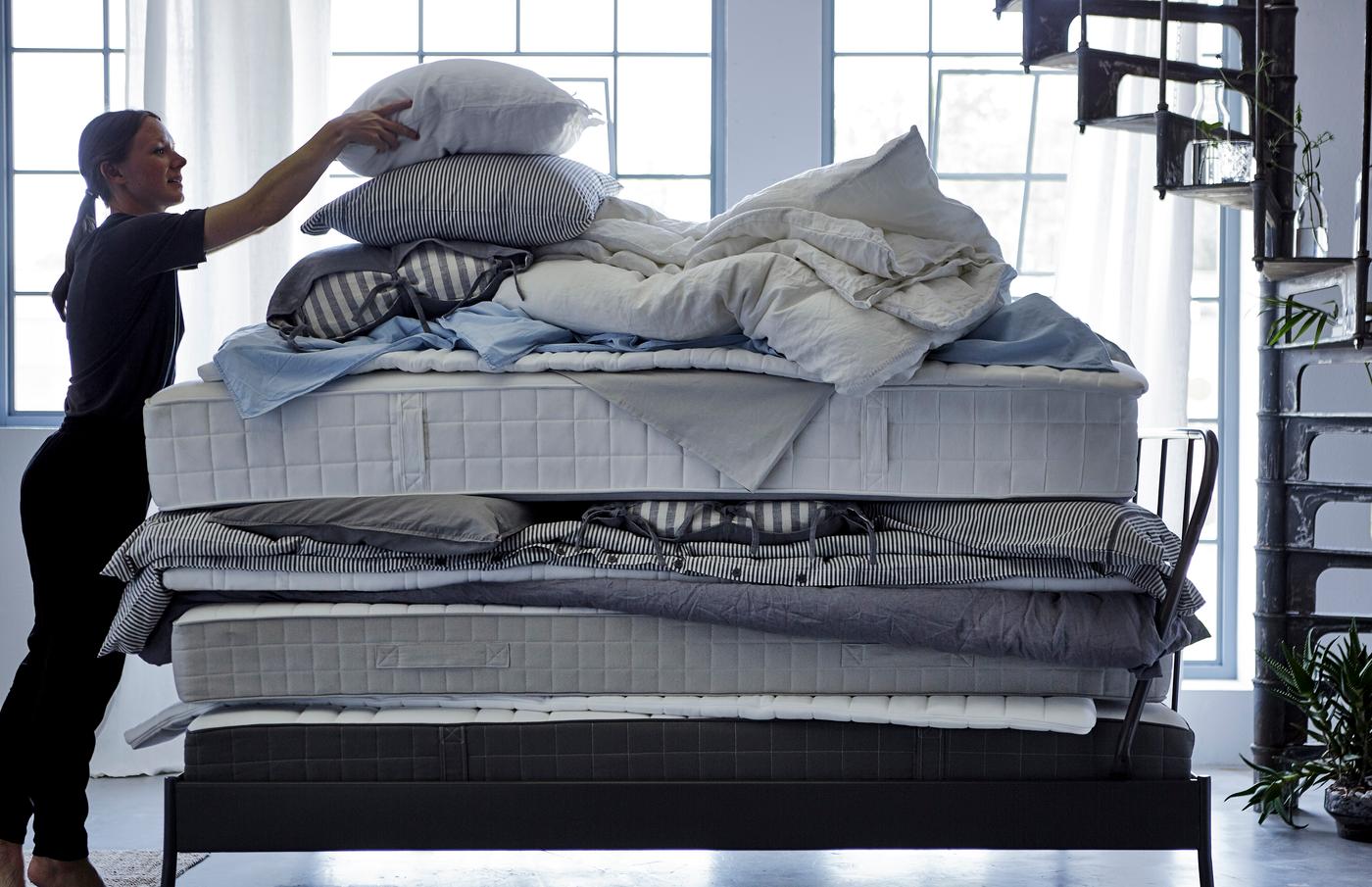 Femme en train de poser un oreiller sur une pile de matelas, couettes et linge de lit.