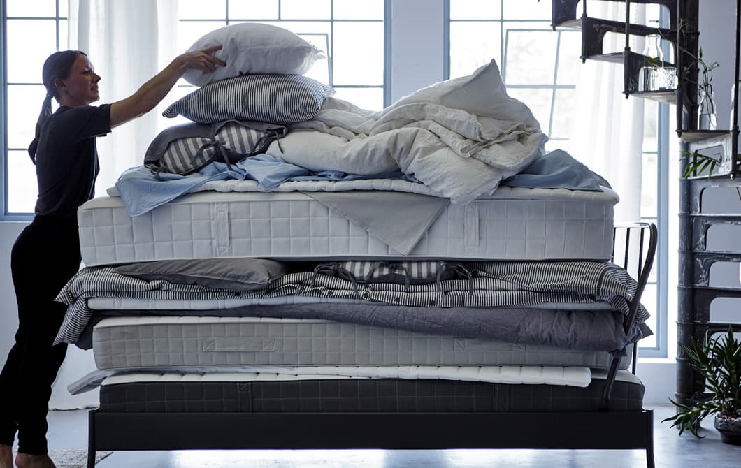 Femme en train de poser un oreiller sur une pile de matelas, couettes et linge de lit