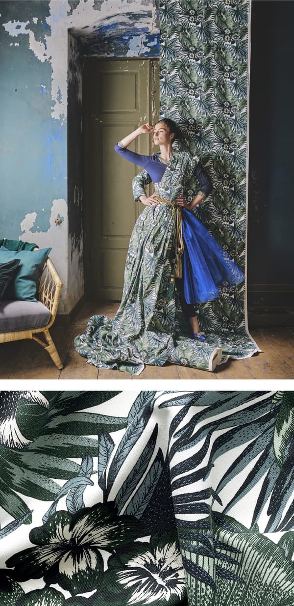 Femme posant drapée dans un tissu à motif botanique dont un lé est suspendu au mur.