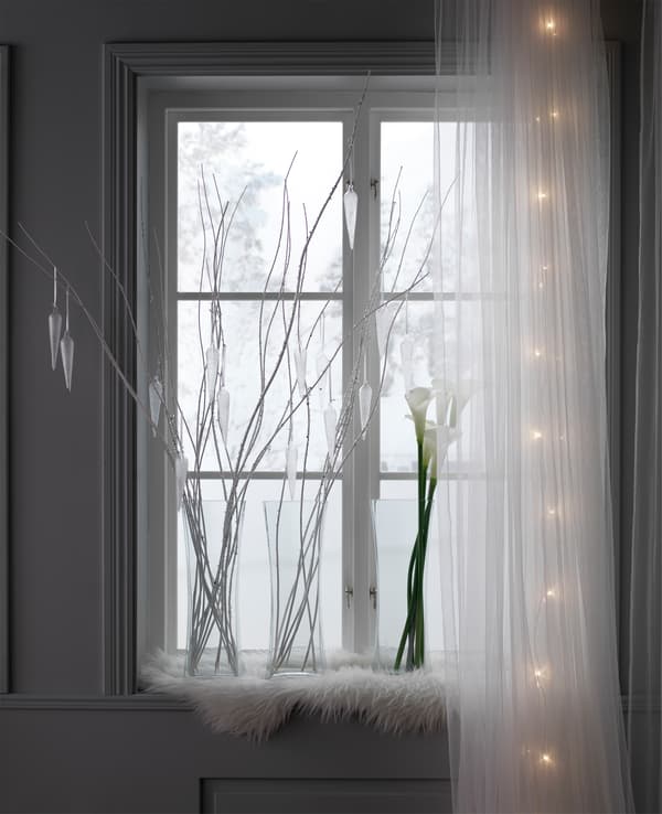 Fenêtre donnant sur un décor enneigé, décorée de vases en verre, de rameaux et d'arums.