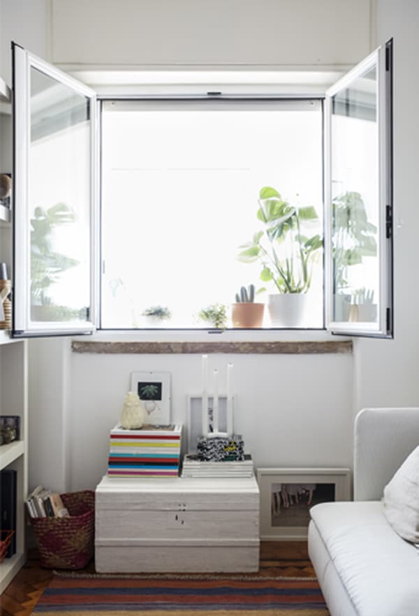 Fenêtres grandes ouvertes sur un séjour blanc décoré d’un tapis à rayures.