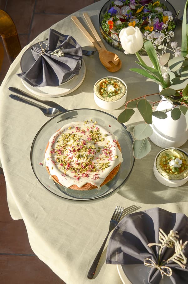 Festive table with cake, salad with flowers, dips, tulips and cutlery on light tablecloth.