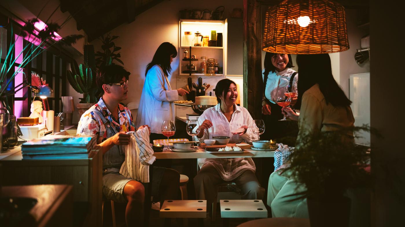 Five people around a set of 4 black/birch effect FRIDNÄS nesting tables with stools below a KAPPELAND pendant lamp shade.