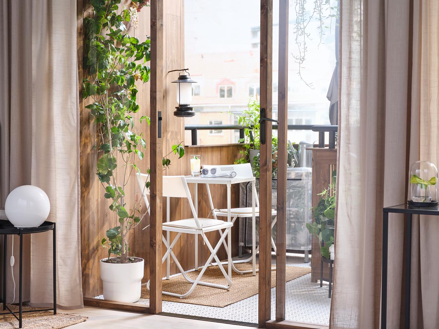 Floor-to-ceiling sliding glass doors, framed by SILVERLÖNN curtains, opening onto a balcony with two FEJAN foldable chairs.