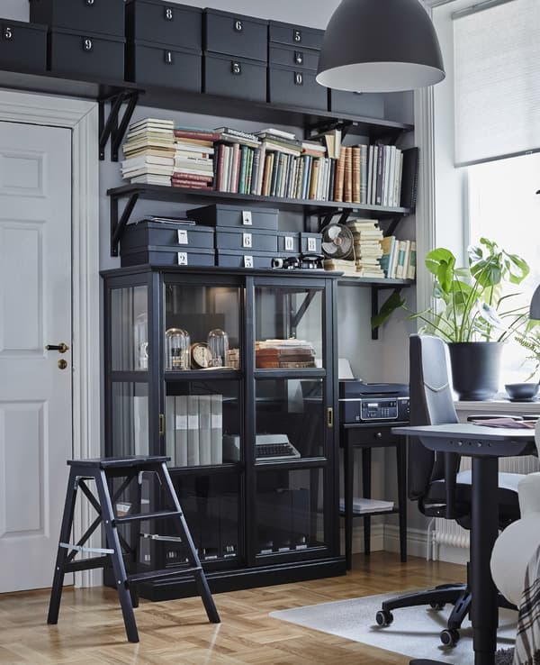 Floor to ceiling storage in a home office. A black step-stool makes it possible to reach the top of the shelving unit.