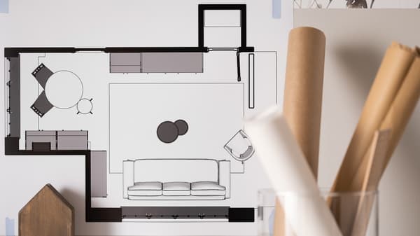 Floorplan of a living room and dining room next to rolls of paper in a glass vase. 