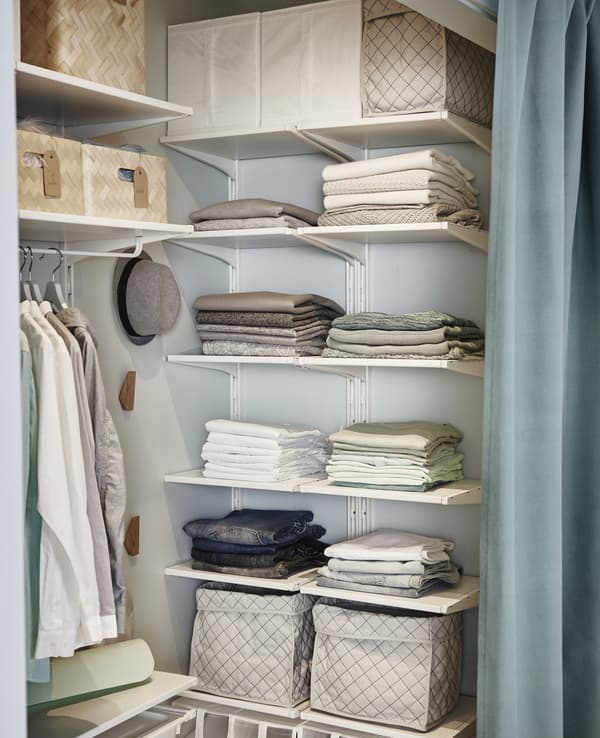 Folded clothes and boxes on adjustable open ALGOT shelves inside a small walk-in closet.