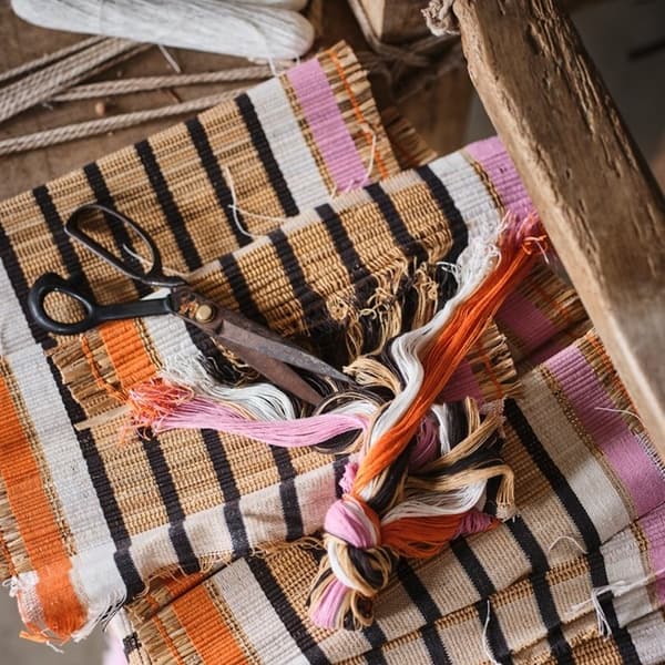 Folded striped MÄVINN place mats and table-runners, neatly stacked with yarns and scissors on top.