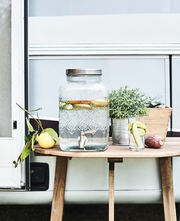 Fontaine en verre avec robinet et citrons sur une table en bois.