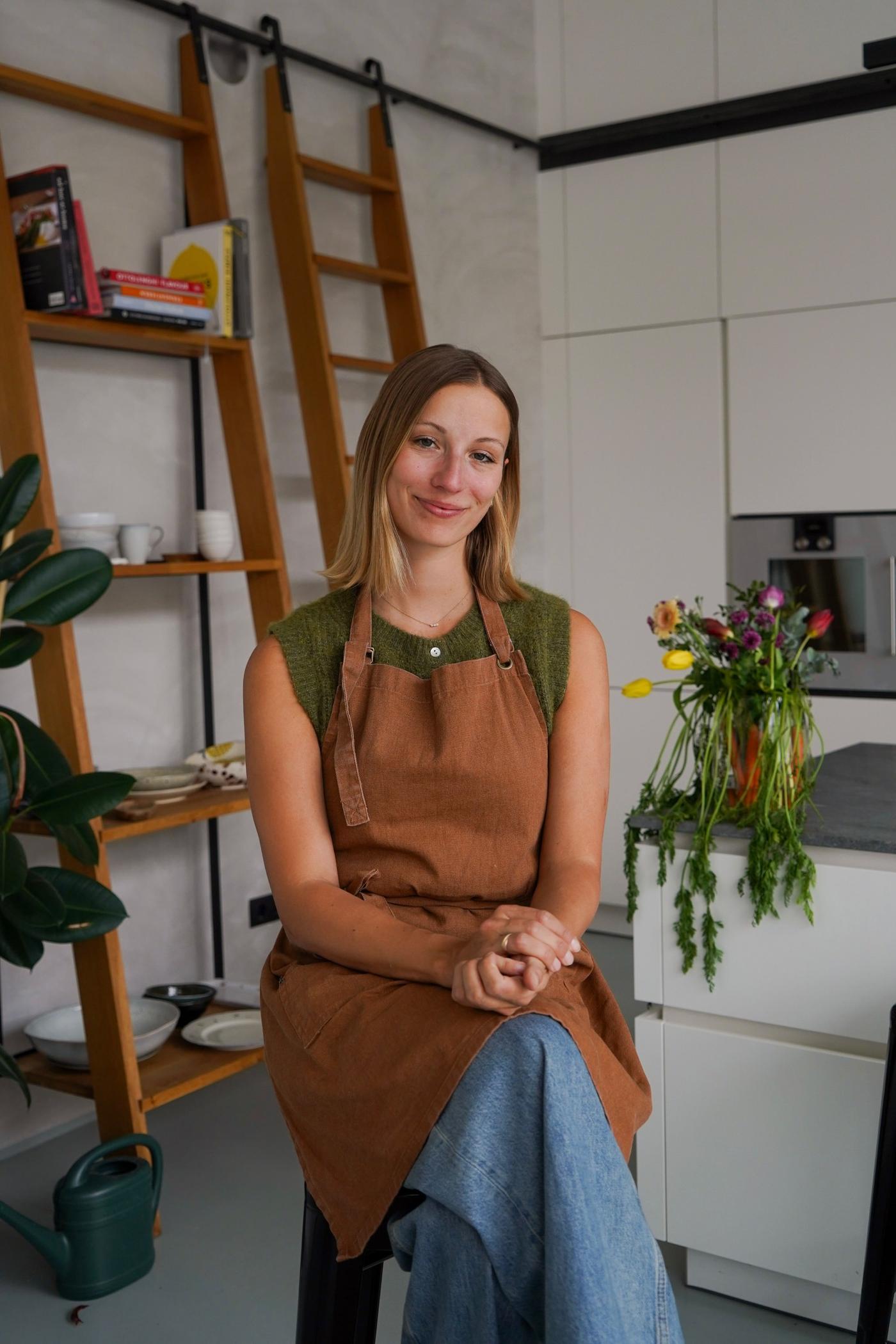 Food-Influencerin @_kirstenclaudia, die in einer Küche auf einem Hocker sitzt