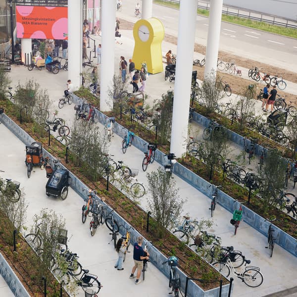 Foran indgangen til IKEA København er der mange cykel parkeringspladser nogle af pladserne holder der cykler på og foran nogle andre pladser står mennesker.