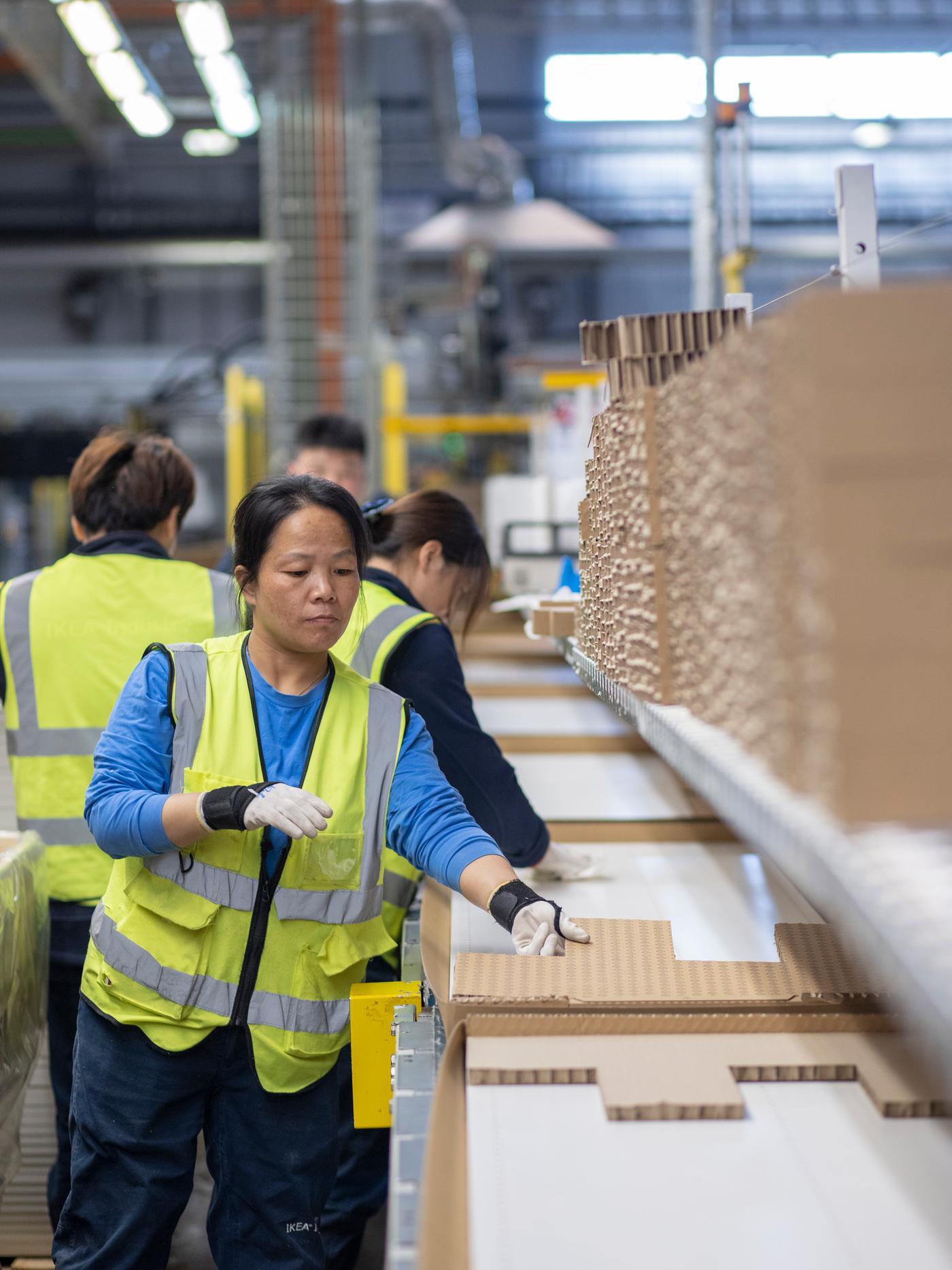 Four Asian workers wearing high-viz vests packing products on an IKEA supplier factory assembly line.