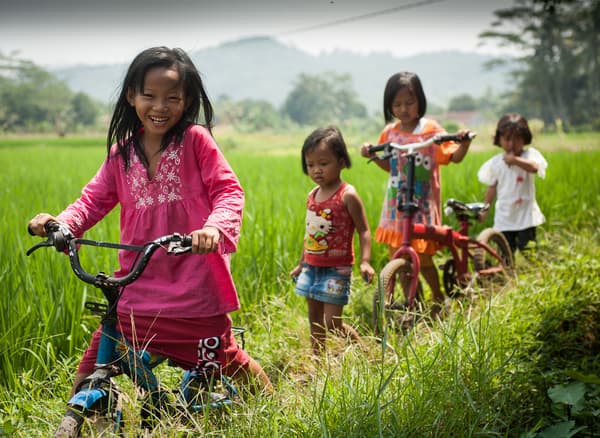 Four children playing and riding bikes in a field.