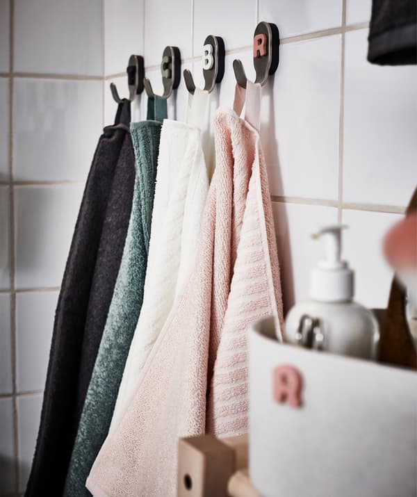 Four different coloured towels hanging from four bathroom hooks in a white tiled bathroom.