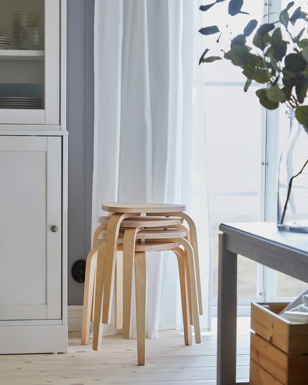 Four KYRRE stools in birch are stacked by a window, and they provide more seating by the dining table when it's extended.