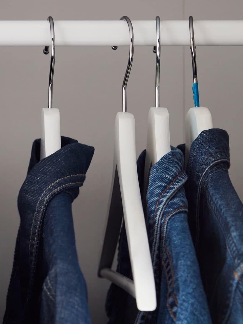 Four white hangers hang from a metal rod, each holding a pair of blue jeans, set against a neutral background.