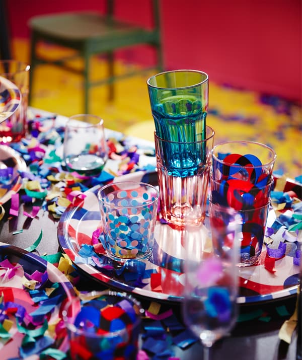 FRAMKALLA and POKAL glasses in red and blue, set on a table scattered with confetti.