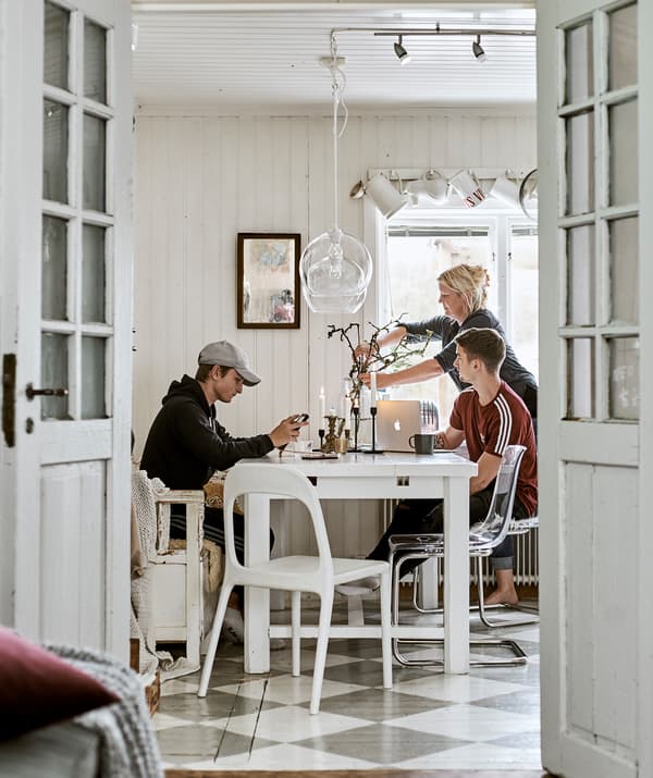 French doors open to a dining room with checked floor. A family sits at a white dining table, glass lamps hang overhead.