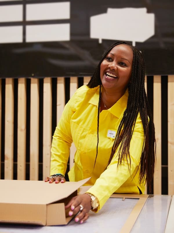 Freundliche IKEA Mitarbeiterin in gelber Uniform verpackt ein Produkt an einem Packtisch im Einrichtungshaus.