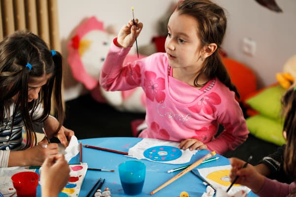 Fröhliche Kinder beim kreativen Malen und Basteln an einem blauen Tisch – IKEA Kinderbereich mit spielerischer Lernatmosphäre und bunten Bastelmaterialien.

