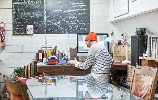 Gareth assis à son bureau avec des livres, un ordinateur et une lampe de bureau avec un tableau noir accroché au mur.