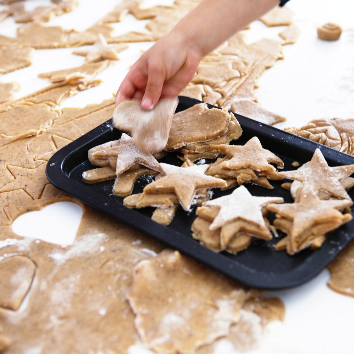 Gingerbread cookies fressh out of the over on a table,  where more cookies are being prepared. 