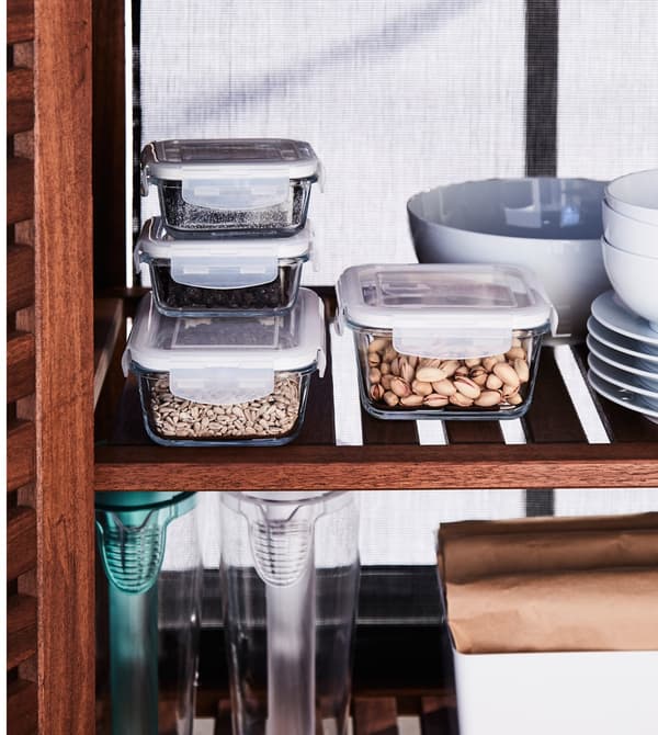 Glass food storage containers and white tableware stored on wooden cabinet shelves.
