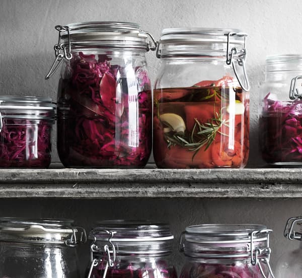 Glass jars on a shelf filled with pickled cabbage and red peppers.
