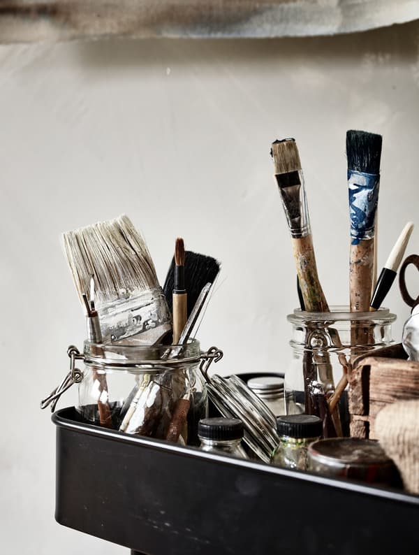 Glass jars storing paint brushes sitting in a metal trolley.