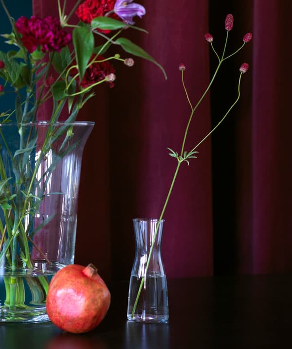 Glass vases with simple flower arrangements shown against a deep rich red curtain.