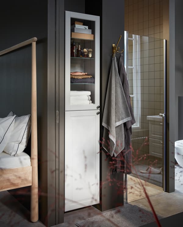 GODMORGON high cabinet in white with a white door and a glass door. Towels and shaving products are stored inside.